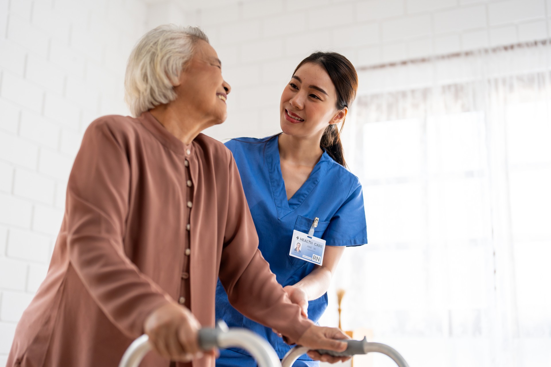 Asian senior older woman patient doing physical therapy with caregiver. Attractive specialist carer women help and support elder mature female practice walking slowly with walker at nursing home care.