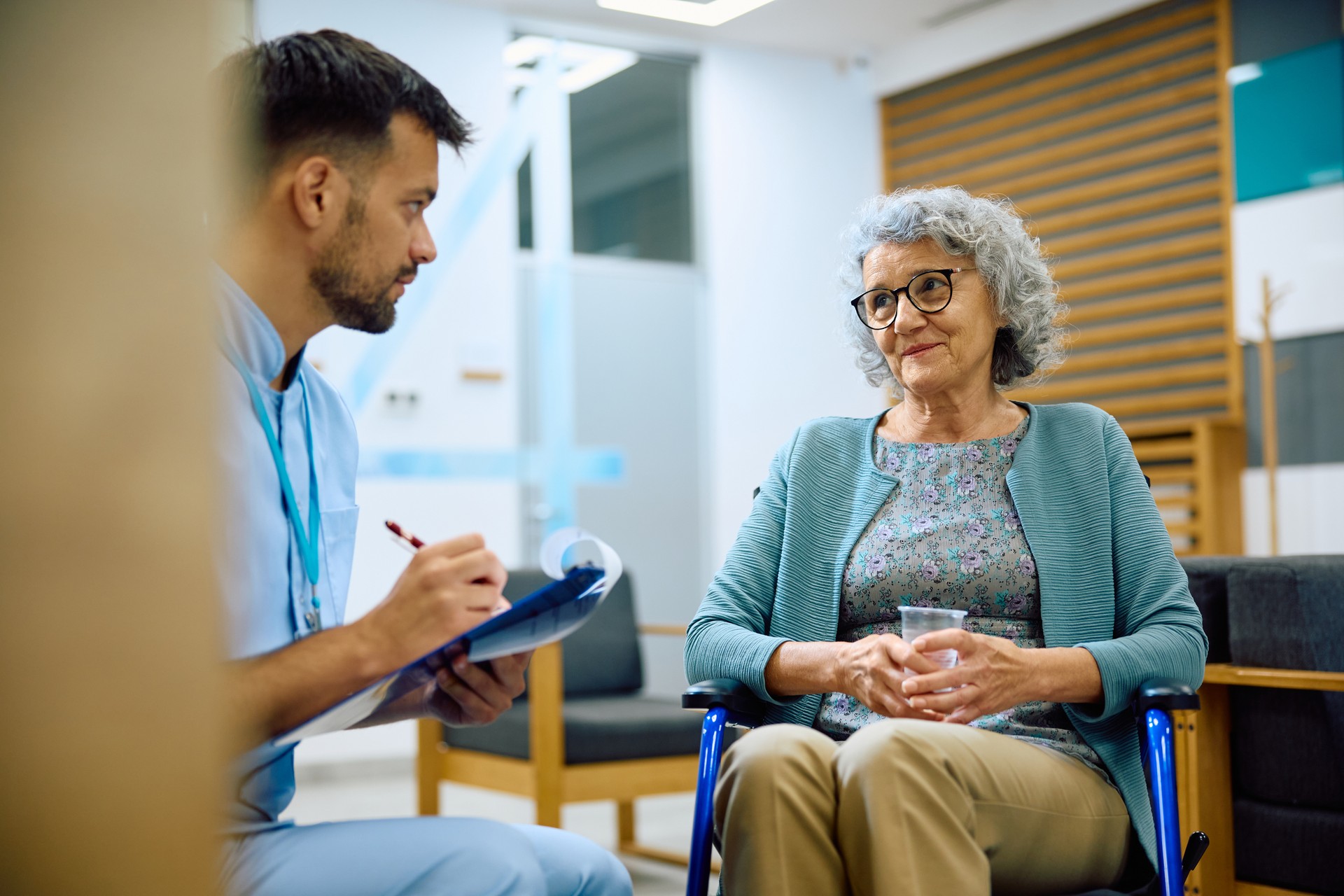 Senior woman talking to male nurse in waiting room at doctor's office.